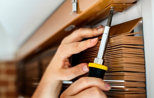 A window blind being repaired by removing the headrail bracket with a Phillips screwdriver