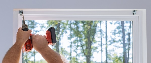 A person using a powerdrill to install brackets in a window recess