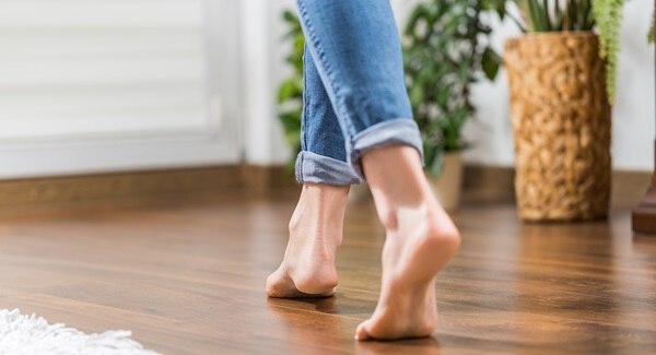 Young woman walking in the house barefoot to ground herself, gently making her way across the wooden panels to her houseplants.
